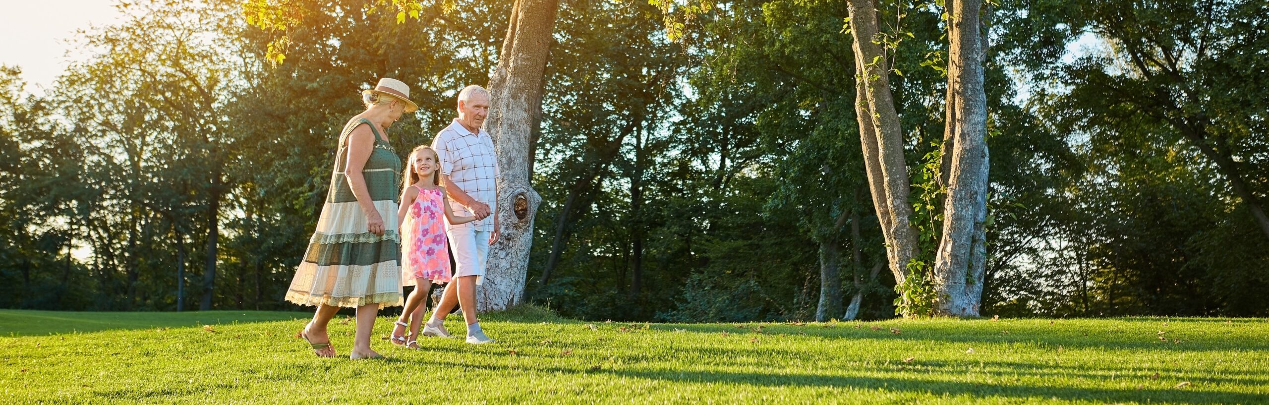 Seniors with granddaughter walking outdoors. People in summer.